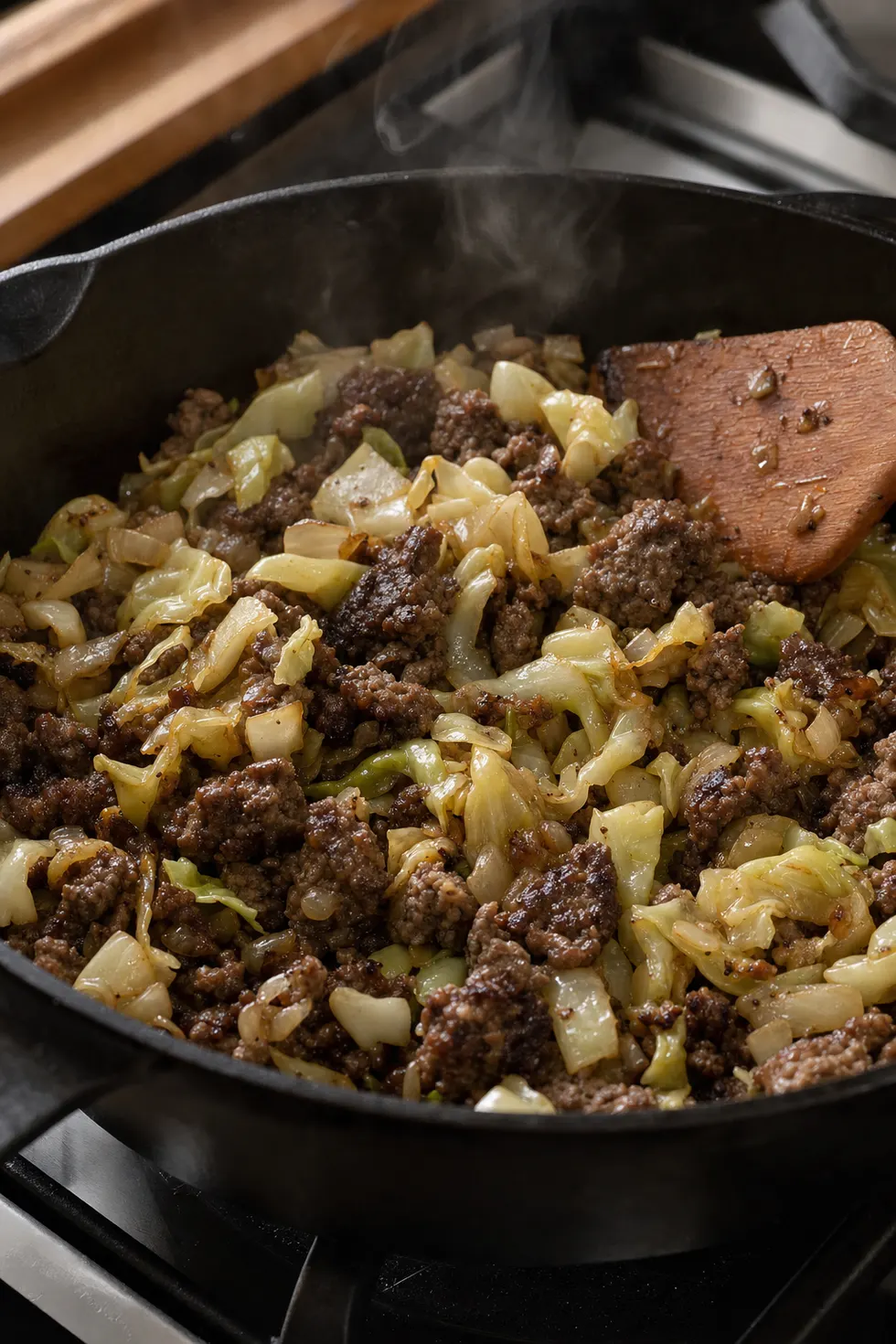 Beef and cabbage cooking together mid-stir, browned edges, steam rising from the skillet