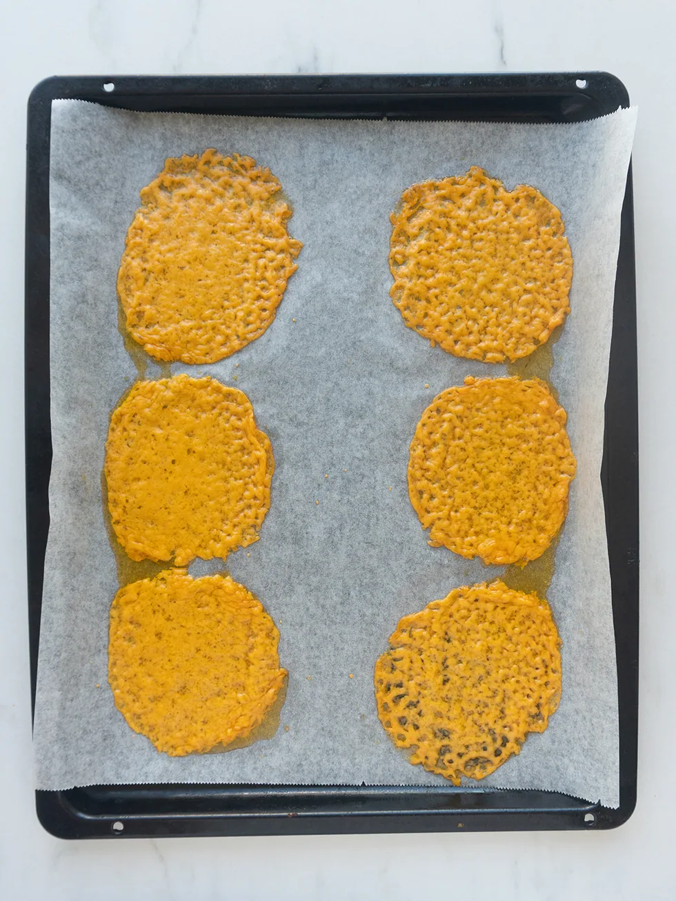 Baked cheddar rounds cooling on a parchment-lined baking sheet, edges lightly browned