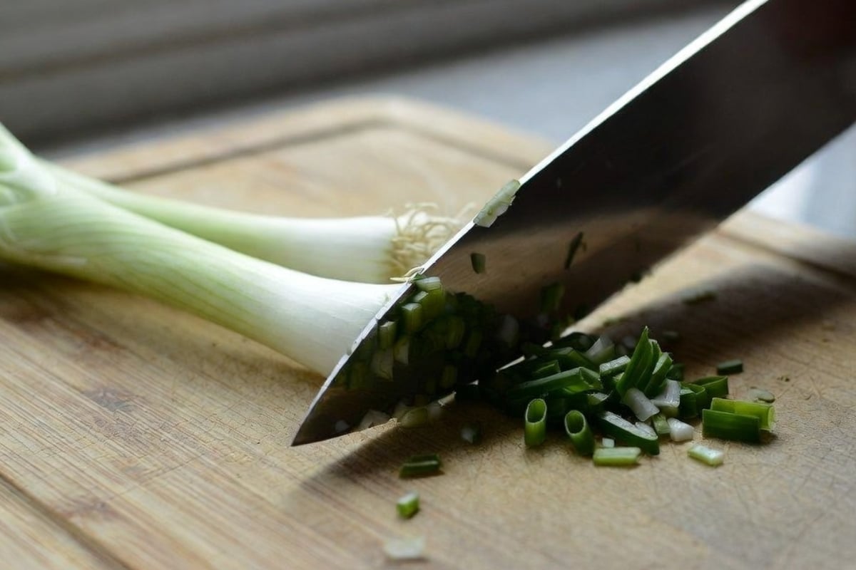 Finely chopping two spring onions on a cutting board for low-carb bacon macadamia spread