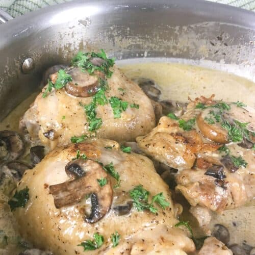 Keto chicken thighs with creamy mushroom sauce in skillet, topped with fresh parsley
