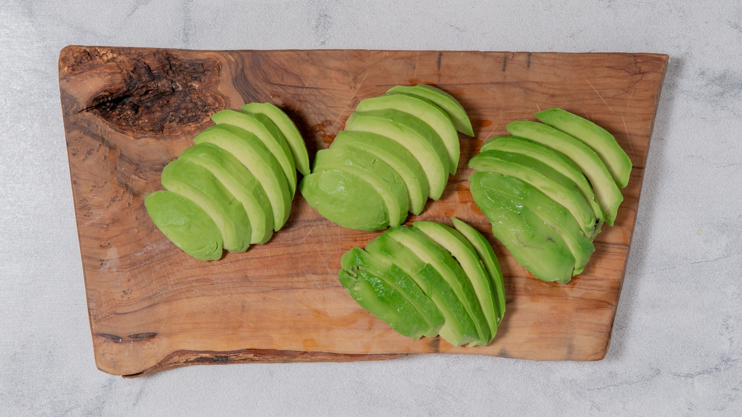 Avocado halves sliced into wedges on a wooden cutting board preparing baked avocado fries