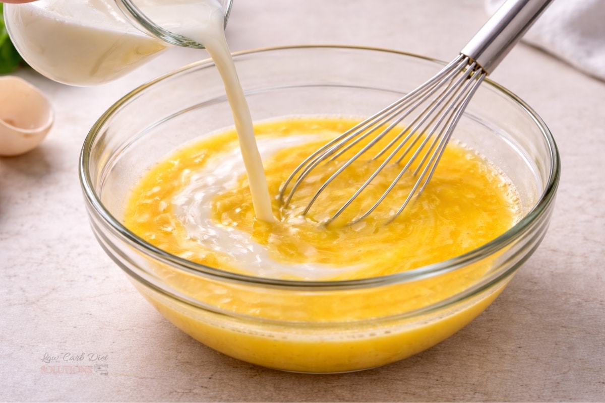 milk being poured into whisked eggs in bowl creating smooth mixture