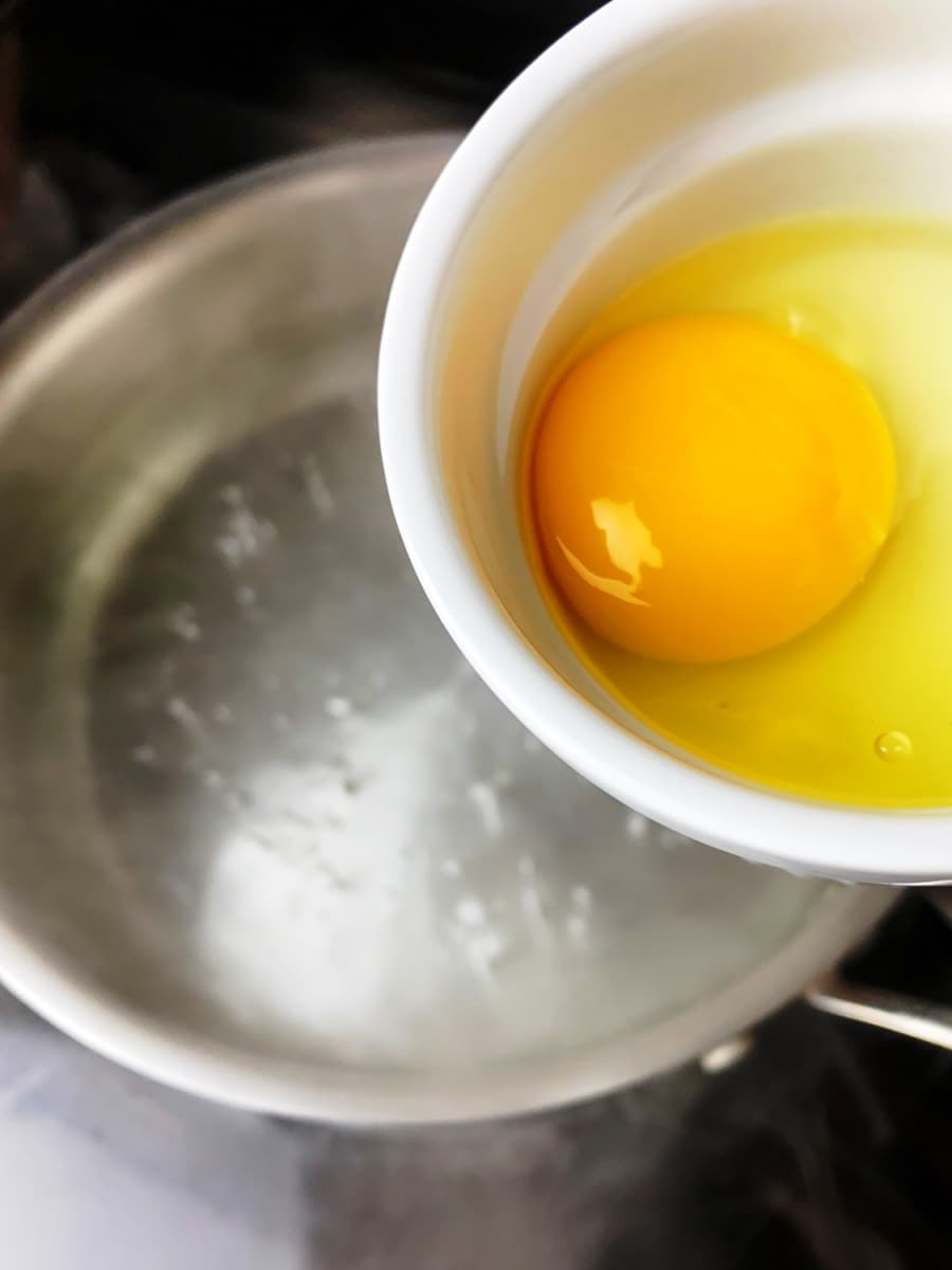 cracked egg in a small bowl ready for poaching in low-carb eggs benedict with spinach