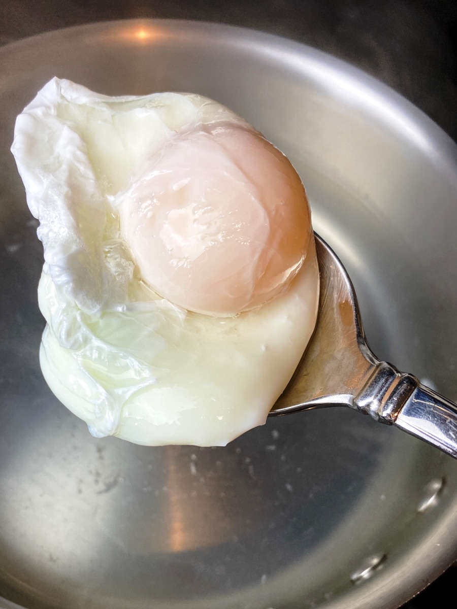 poached egg being removed from simmering water with a slotted spoon