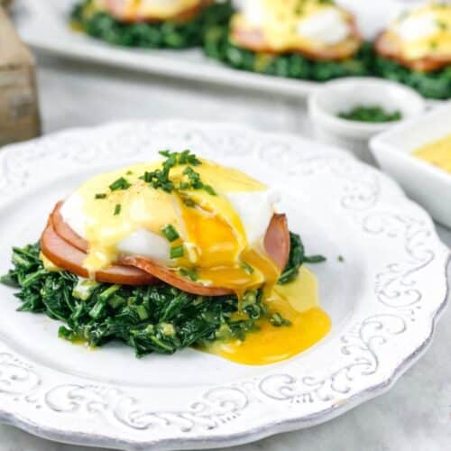 Low-carb keto eggs benedict served on sautéed spinach with Canadian bacon, poached egg, and creamy hollandaise sauce on a white plate