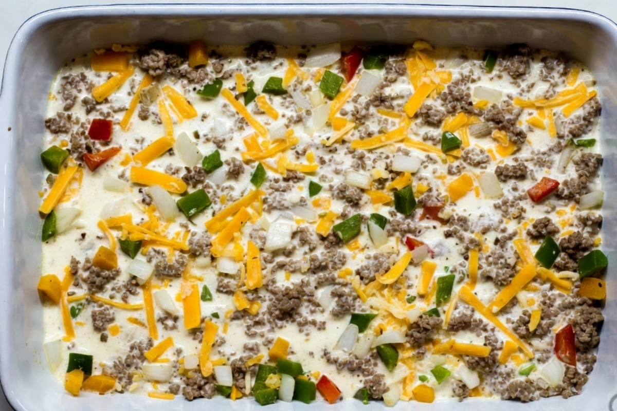 Uncooked sausage and egg breakfast casserole mixture in a 9x13 baking dish with cheese, peppers and onion evenly distributed