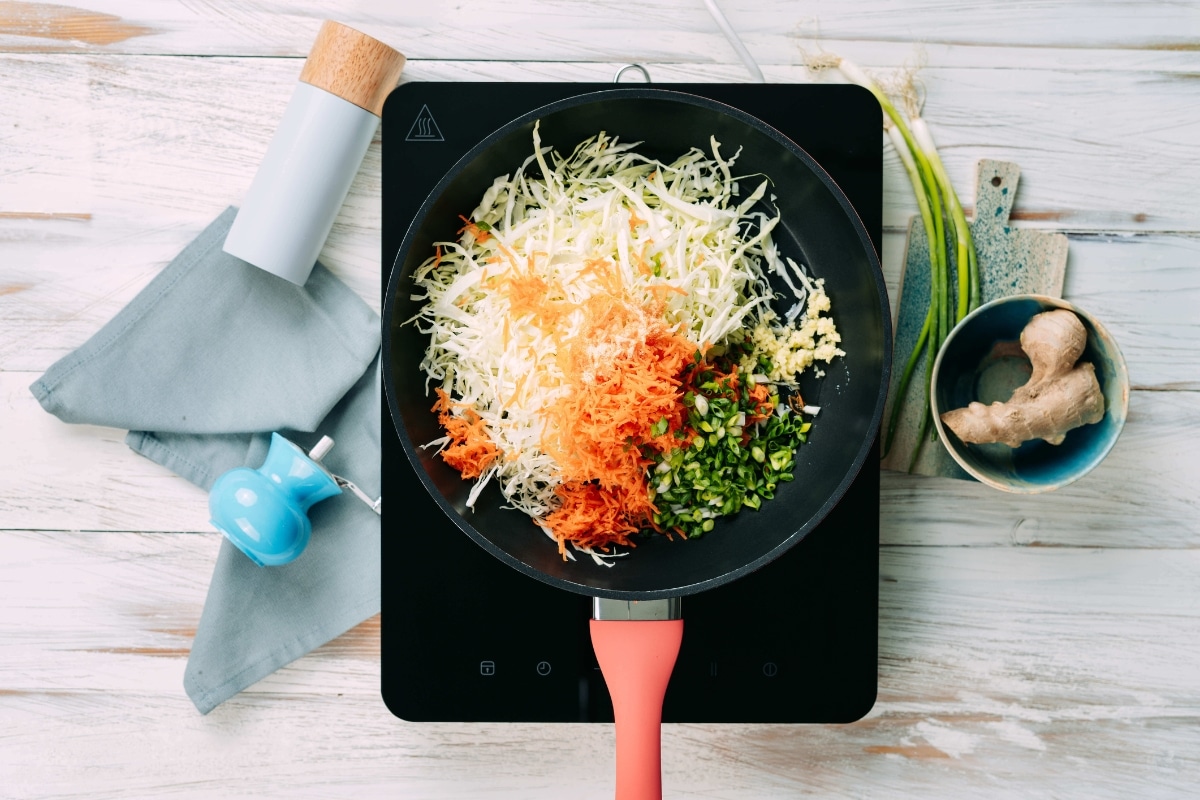 Coleslaw mix, carrots, green onions, and seasonings added to a skillet for low-carb egg roll in a bowl recipe