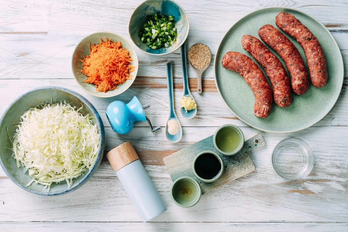 Ingredients for low-carb egg roll in a bowl including sausage, shredded cabbage, carrots, green onions, sesame seeds, and sauces before cooking